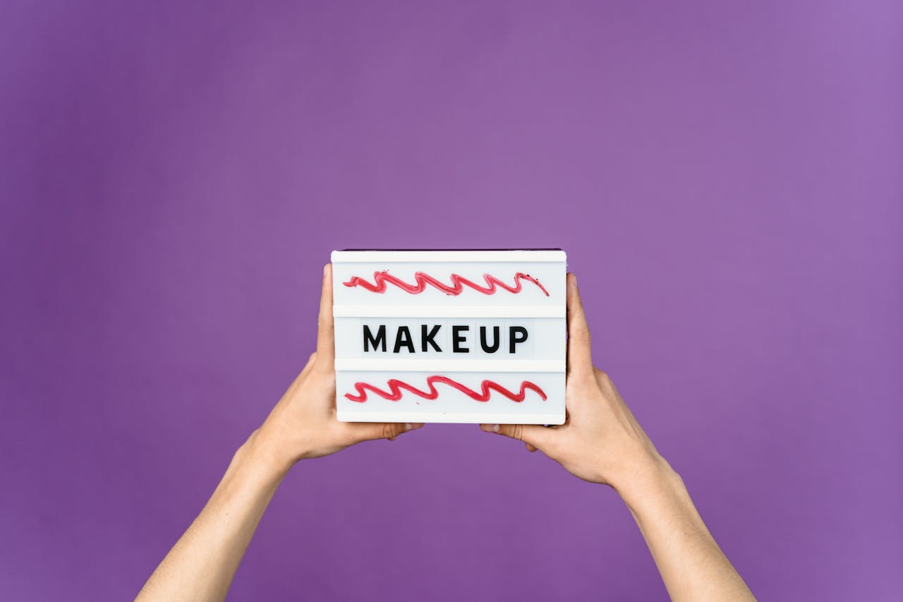 about-02 Close-up of hands holding a lightbox with 'MAKEUP' sign against a purple background.