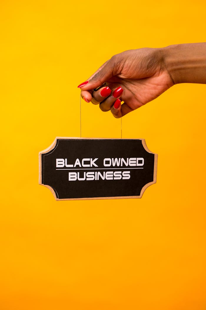 our-experience A hand holds a Black Owned Business sign against a vibrant yellow background.