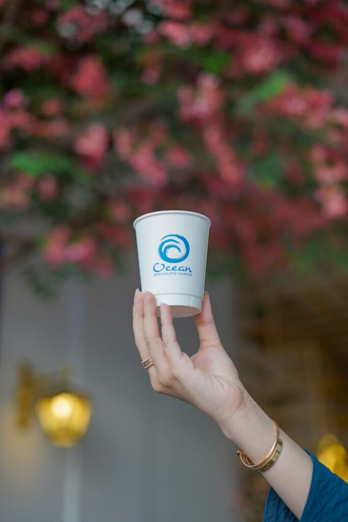 A stylish hand holds a branded cup against a vibrant floral backdrop, highlighting branding.